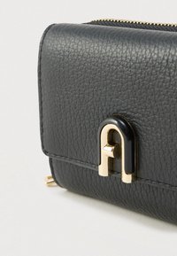 Čierna textúrovaná kožená peňaženka so zlatou kovovou výstužou a výrazným čierno-zlatým zapínaním, ktorá má zips pozdĺž hornej hrany.