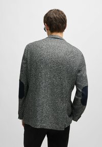 Blazer grigio a spina di pesce con rever a contrasto, dotato di toppe sui gomiti scure e una finitura testurizzata. La vista posteriore mostra una fessura singola.