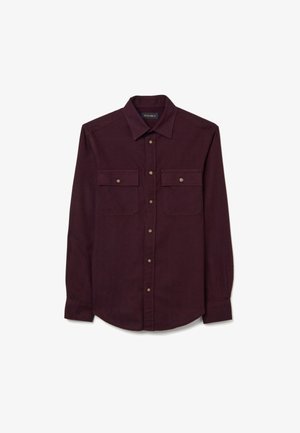 Bordeauxrode longsleeve gemaakt van zachte stof, met een knoopsluiting aan de kraag, twee borstzakken en ronde knopen.