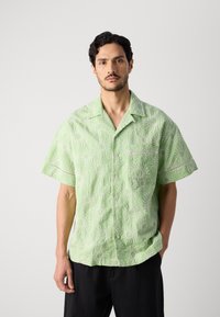 Light green short-sleeve shirt with embroidered sunburst patterns, button closure, and a chest pocket. Casual fit with a relaxed texture.