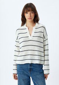 Maglione bianco lavorato a maglia con righe orizzontali blu, colletto a V e maniche lunghe. Abbinato a jeans blu. Tessuto strutturato.