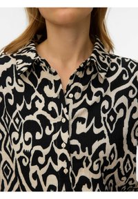 Femme portant une chemise à boutons à motifs noir et blanc avec un col, montrant la partie supérieure de la poitrine et le cou.
