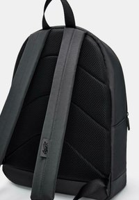 Sort rygsæk med polstret mesh ryg, justerbare stropper og tekstureret materiale. Har en sidelomme med lynlås og et logo-mærke på stroppen.