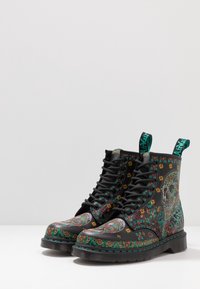 Botas de combate de cuero negro con patrones coloridos de flores y calaveras, diseño con cordones y detalles en verde en los ojales y la suela.