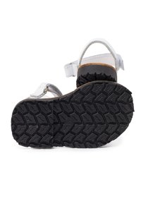 White leather sandal with a black rubber sole, featuring a textured tread pattern and adjustable straps for a secure fit.