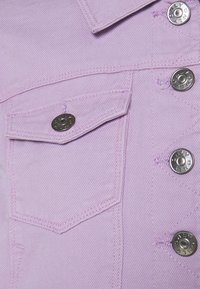 Ljuslila denimjacka med silverfärgade tryckknappar, en bröstficka och synliga sömdetaljer. Texturen är jämn och strukturerad.