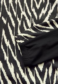 Czarno-białe tkaniny w zygzakowaty wzór o gładkiej fakturze, z solidnym czarnym mankietem na krawędzi.