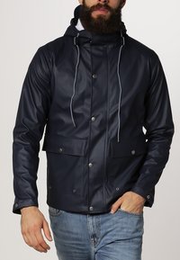 Marinblå vattentät jacka med huva, två framfickor, tryckknappar och dragsko detaljer; stilren, slät och modern design.