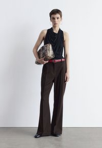 Schwarzes ärmelloses Top, lockere Passform; braune hochgeschnittene Hose; roter Gürtel; Clutch im Schlangenmuster; graue Schuhe; schlichter Hintergrund.