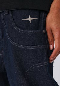 Dark denim jeans with a subtle texture, featuring silver hardware detail in the shape of a star on the back pocket.