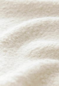 Soft, off-white fabric with a textured, fuzzy surface, displaying gentle waves and folds, highlighting its plush material and light shade.