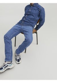 Camisa de mezclilla y jeans en tonos de azul; diseño estructurado con cierre de botones. Zapatillas blancas y marinas con acentos de malla y goma.