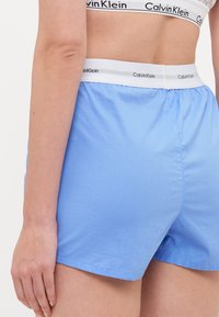 Svijetloplave pamučne kratke hlače s elastičnim pojasom i bijelim Calvin Klein logotipom. Glatka tekstura i ležeran kroj za udobnost.