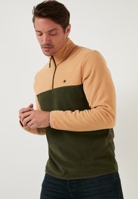 Fleece pulover u boji kestena i tamnozelene, s polu-zip ovratnikom, dugim rukavima i malim logom na prsima. Ukupno mekana tekstura.