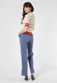Knitted striped top in cream, red, and blue; paired with tailored light blue pants featuring side slits and black high-heeled shoes.