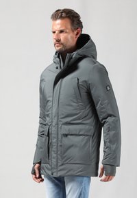 Pelēks izolēts jārts ar kapuci, priekšējo rāvējslēdzēju un divām lielām kabatām. Iespējotas pieguļošas aproces un smalks logotips uz piedurknes. Gluda tekstūra.