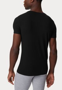 T-shirt nera a maniche corte in cotone liscio, con un classico collo a giro e un design aderente, abbinata a pantaloni grigi chiari.