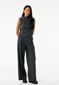 Pull en tricot à col haut sans manches gris foncé, associé à un pantalon large en charbon et des chaussures noires chunky.