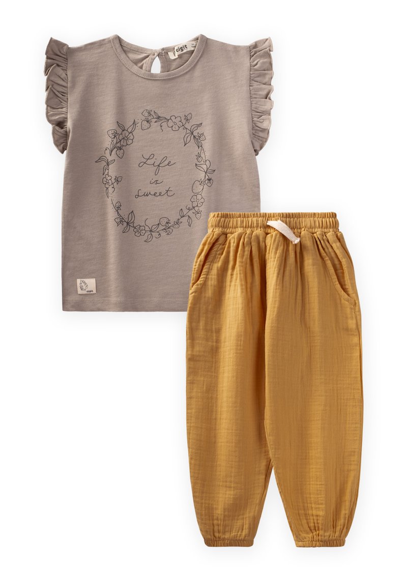 Graues Kurzarmhemd mit Rüschenschultern und floralen Motiven; kombiniert mit gelben Baumwollhosen mit elastischem Bund und Taschen.