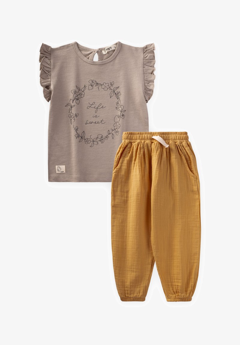 Grijze kortekorte mouw shirt met gerimpelde schouders en bloemenpatroon; gecombineerd met gele katoenen broeken met een elastieken tailleband en zakken.