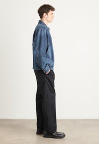 Jachetă din denim bleumarin, cu o croială relaxată, asociată cu pantaloni negri și pantofi negri. Caracteristici de design simple și siluetă dreaptă.