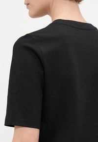 Černé tričko s krátkým rukávem vyrobené z hladké látky, s kulatým výstřihem a čistým, minimalistickým designem.