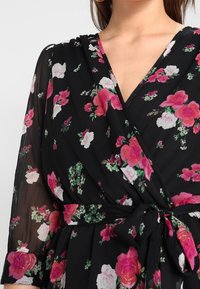 Svart blommig omlotklänning med rosa och vita rosor, med v-ringning, knytmidja och genomskinliga långa ärmar. Mjuk, flödande tyg.