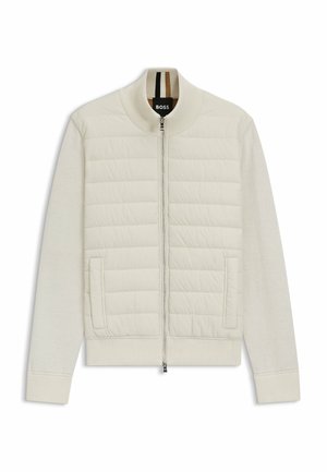 Veste bomber crème clair avec un panneau supérieur matelassé et des manches douces. Comprend une fermeture éclair à l'avant, des poches latérales et des poignets et un col côtelés.