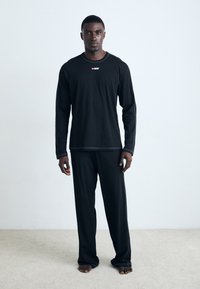 Black long-sleeve top and matching pants made of a soft fabric. The shirt features a small red logo on the chest. Simple and relaxed fit.