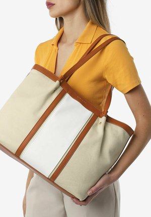 Grote schoudertas gemaakt van beige textuurstof met witte en bruine leren accenten, voorzien van twee bruine hengsels en een rits bovenaan.