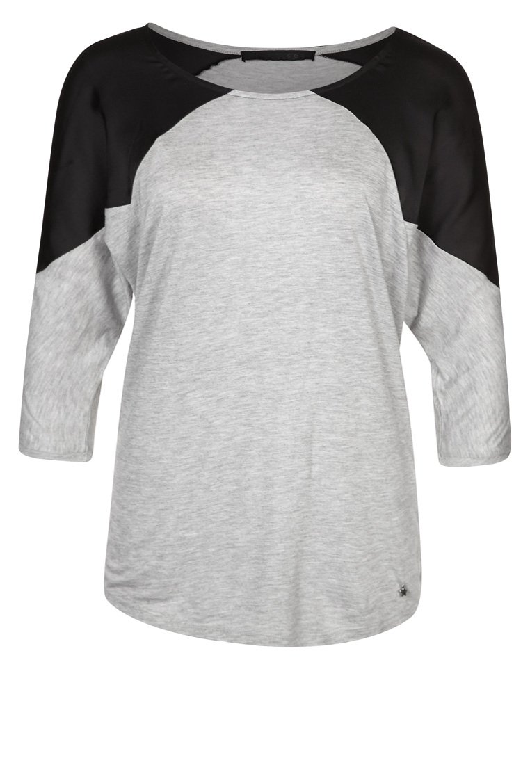 Top de manga tres cuartos en gris y negro con un escote redondo, que presenta paneles de tela contrastantes y una textura suave. Pequeño logo en el dobladillo.