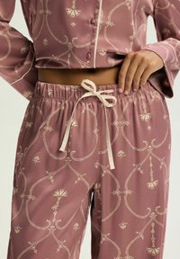 Różowy satynowy zestaw piżamowy z wzorzystym designem i kremowymi akcentami. Koszula z guzikami; spodnie z elastycznym pasem i sznurkiem do regulacji.