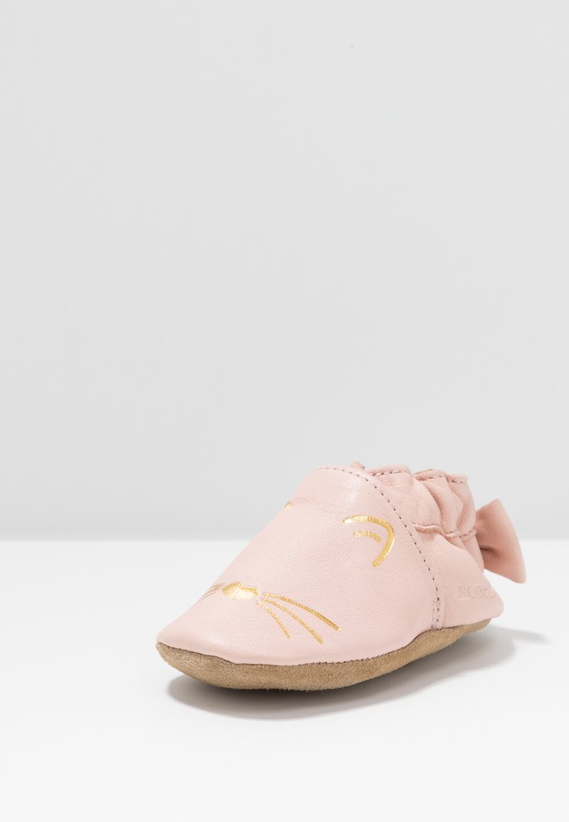 Rosa lærbabysko med rund tå, dekorert med gull whisker-design og en liten sløyfedetalj. Myk, fleksibel såle for komfort.