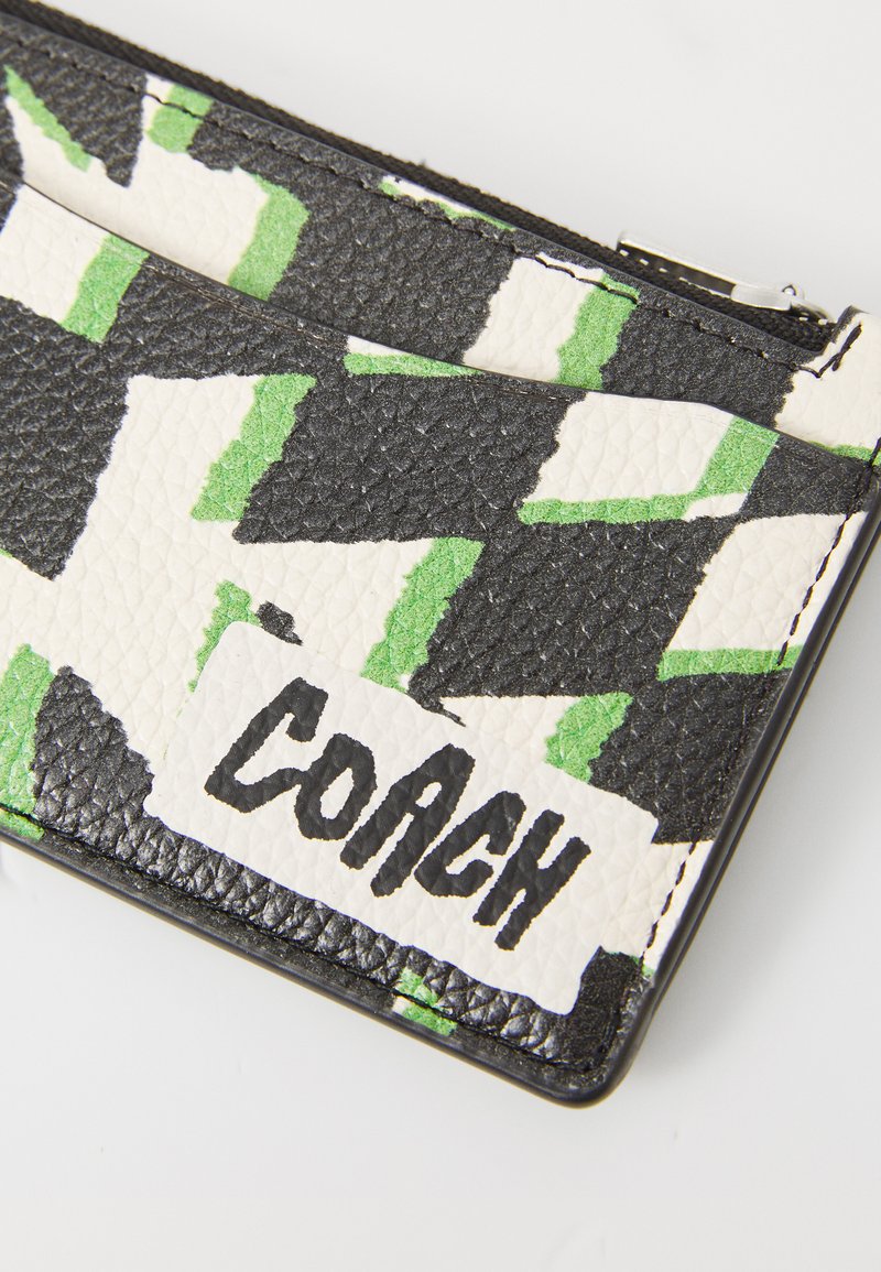 Leather cardholder in black, white, and green with a geometric pattern and a prominent white logo displaying "COACH." Textured surface.