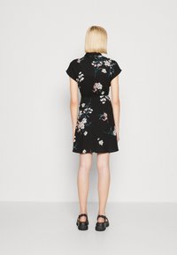 Schwarzes Blumenkleid mit kurzen Ärmeln, tailliertem Schnitt und lockerem Sitz. Mit weißen und pinkfarbenen Blumen auf schwarzem Hintergrund gestaltet.