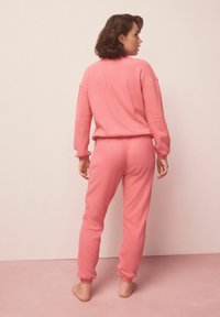 Ružová súprava na doma z mäkkej látky; top má voľný strih s dlhými rukávmi a nohavice majú našité manžety a elastický pás.