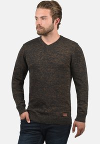 Dunkelgrauer V-Ausschnitt-Pullover mit braunen Sprenkeln. Strukturiertes Strickmaterial und gerippte Bündchen. Gesticktes Logo-Patch in der Nähe des Saums.