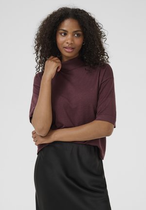 Haut bordeaux à manches courtes avec un col montant, fabriqué en tissu texturé. Accompagné d'une jupe en satin noir, mettant en valeur une coupe décontractée.