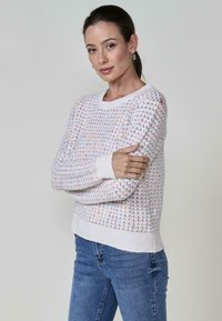Fehér kötött pulóver színes csillagmintákkal, bordás mandzsettákkal és szegéllyel, laza szabással és puha textúrával.