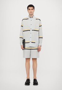 Stripet skjorte i lys grå med blå, svart og gul stripedesign; kombinert med matchende shorts. Svarte sko og en clutch.