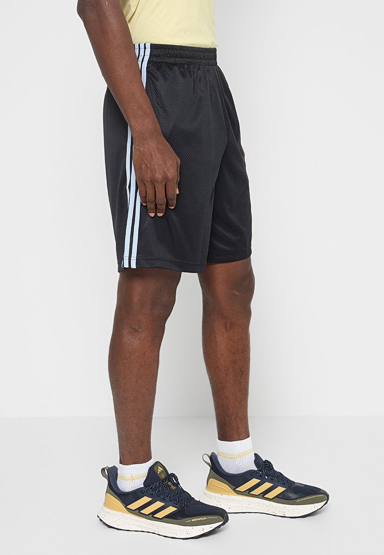 Pantalones cortos deportivos de malla negra con franjas laterales azul claro, cinturilla elástica y un corte relajado, combinados con zapatillas marinas y amarillas.