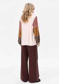 Bluzka z długim rękawem z wzorzystymi rękawami w odcieniach bordowego, musztardowego i zielonego, zestawiona z luźnymi brązowymi spodniami z bocznymi paskami.