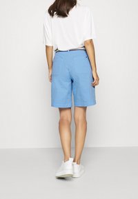 Niebieskie bawełniane szorty o luźnym kroju, z dwoma tylnymi kieszeniami i podwiniętym dołem, w zestawieniu z białą, oversize'ową koszulą i białymi trampkami.