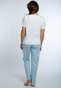 Camicia bianca a maniche corte abbinata a pantaloni leggeri a righe verticali blu. Tessuto morbido con una vestibilità comoda e lunghezza fino alla caviglia.