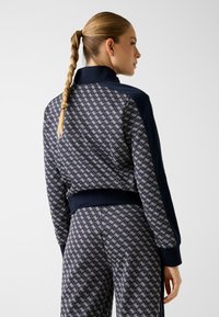 Granatowa bluza dresowa w wzory z prążkowanymi mankietami, z geometrycznym nadrukiem na plecach oraz gładkimi panelami z przodu i na rękawach.