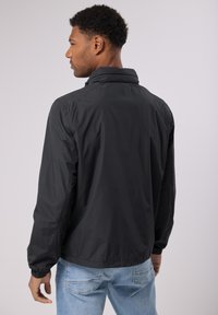 Schwarze, leichte Jacke mit hohem Kragen und elastischen Bündchen, mit glatter Textur und einfachem Design, getragen über hellblauen Jeans.
