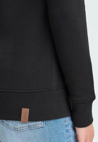 Felpa nera in misto cotone; presenta un orlo e polsini a costine, con una piccola etichetta in pelle marrone sul retro.