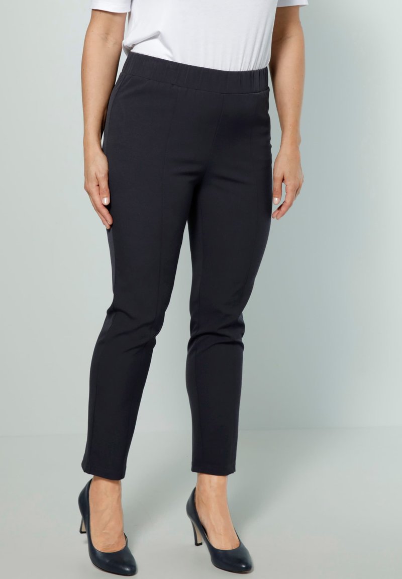 Svarta, stretchiga byxor som dras på med en slät yta, slim fit, längd till anklarna och med resårmidja, kombinerat med mörka högklackade skor.