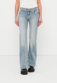 Jean évasé bleu clair en denim, avec une taille mi-haute, deux poches avant, des effets délavés et des accents de coutures.