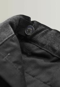 Schwarzer Stoff mit glatter Textur; verfügt über einen glänzenden Knopf und ein elastisches Band oben. Enthält innere Nähdetails.